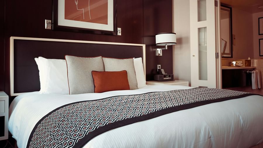 A luxurious hotel bedroom with a large bed, dark headboard, and rich purple accents.