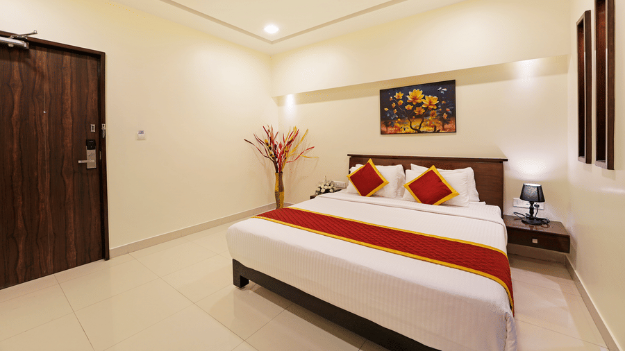 A Premium Room at Clover - A Rivido Hotel, featuring a spacious bed, a floral painting above the headboard, a nightstand, and a decorative vase in a corner.