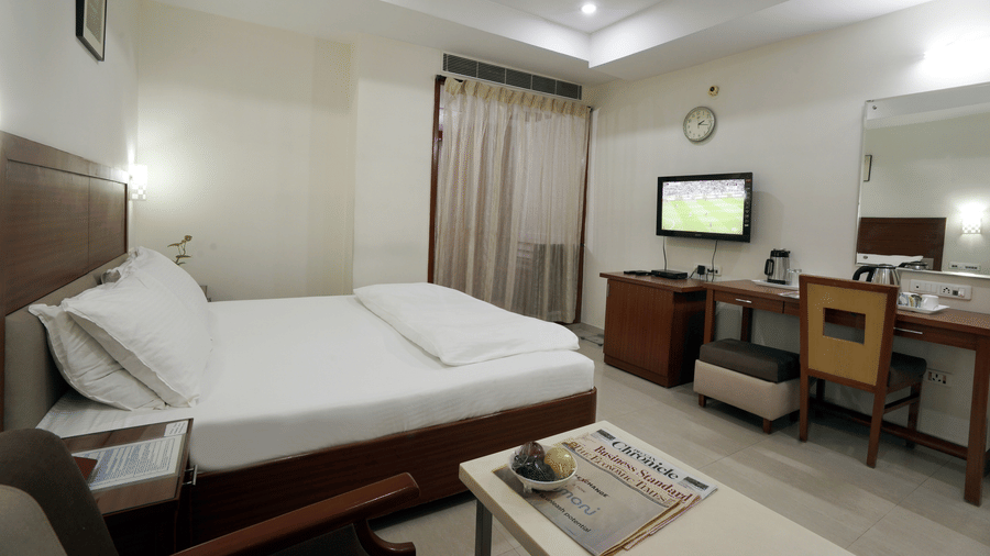 Deluxe room with a comfortable bed, wooden furnishings, television and work desk at Hotel Geetha Regency, Guntur.