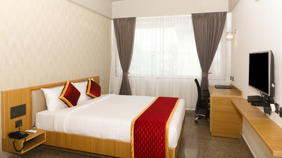 A double bed, a window with curtains, and a wall-mounted television at Icon Express By Bhagini, Mahadevapura.