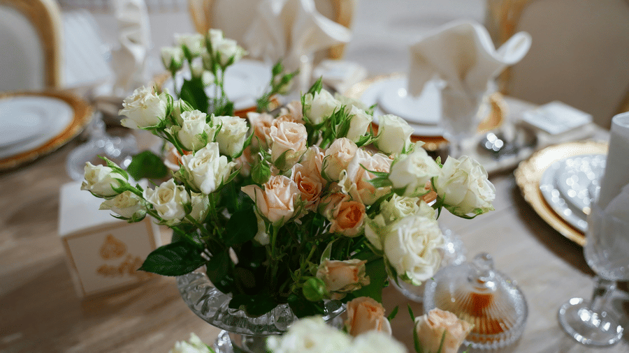 A close up shot of a beautiful flower vase with a lot of white and pink roses on a dining table.