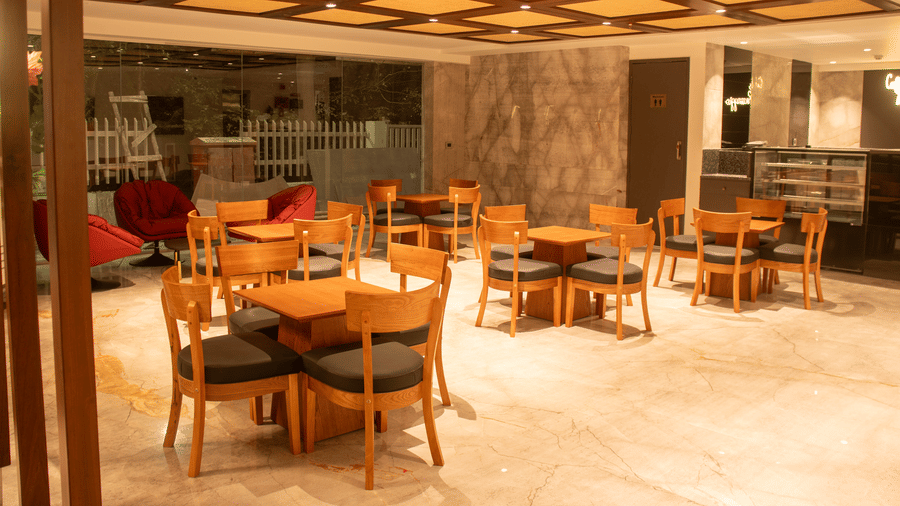 A hotel lobby area with wooden tables and chairs,  cushioned chairs, and ceiling lights arranged in a grid pattern.
