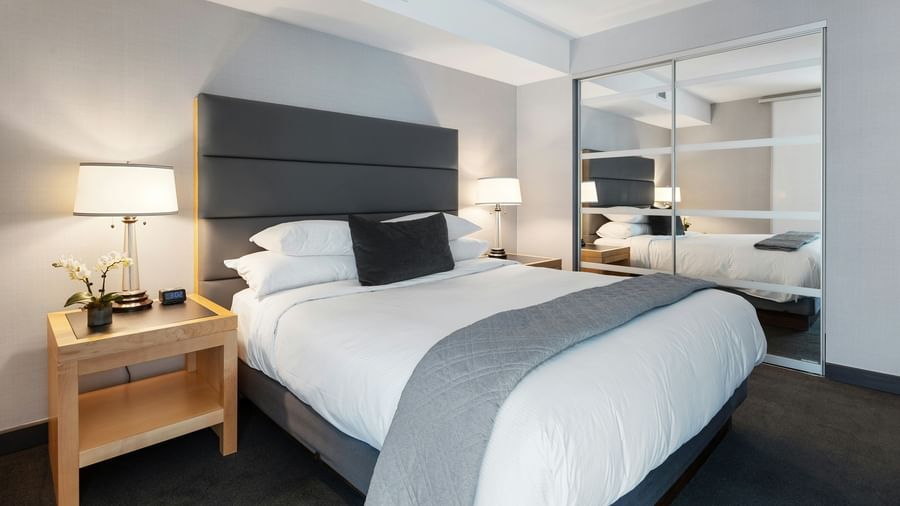 A modern hotel room with a double bed, a table with a lamp beside it and a huge mirror.