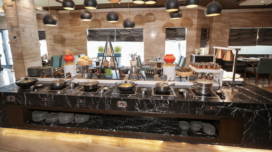 A buffet counter at Park Plaza Ludhiana featuring a dark marble surface with food displays hanging pendant lights and a stone textured wall backdrop in a warmly lit setting.
