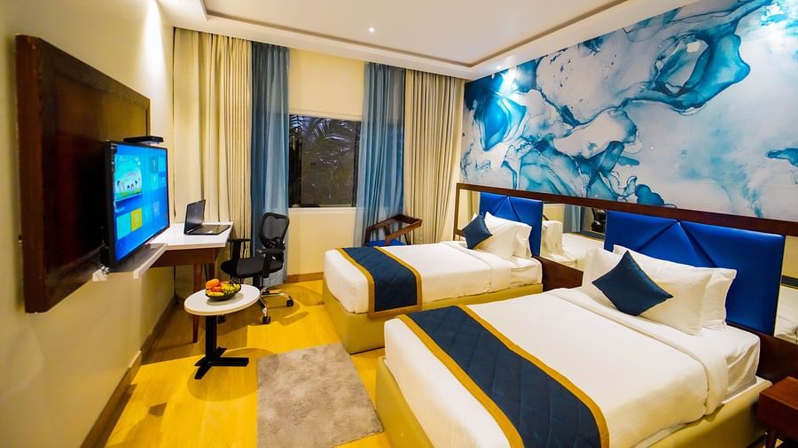 Well-lit twin-bed room with modern interiors, a large TV, workstation, and stylish blue-accented décor at Quality Inn Rockwell Grand, Bangalore.