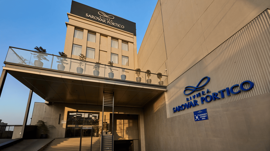 Exterior view of Riviera Sarovar Portico showcasing the main entrance, modern façade, and hotel signage, captured during daylight with a clean architectural perspective.