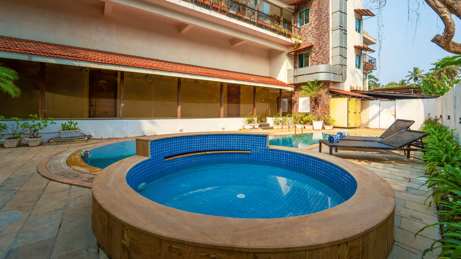 Rosetum Anjuna's circular children's pool with blue mosaic tiles in the foreground, the main swimming pool behind, sun loungers with towels, and the hotel facade in the background.