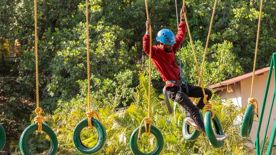 Adventurous individual crossing a tire obstacle course in a lush forest setting. | Stone Wood Jungle Resort, Dandeli