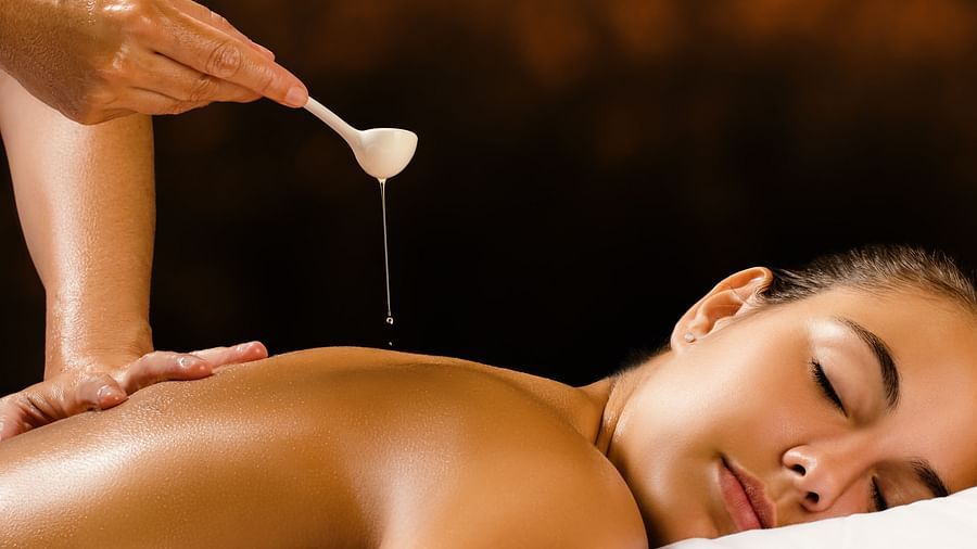 A person receives a liquid treatment on their back with oil dripping from a spoon