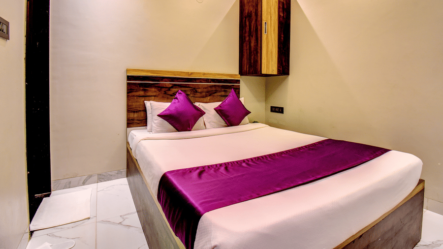 Deluxe Room king bed with purple pillows, wooden headboard and overhead storage cabinet at VITS Select Kharadi Pune