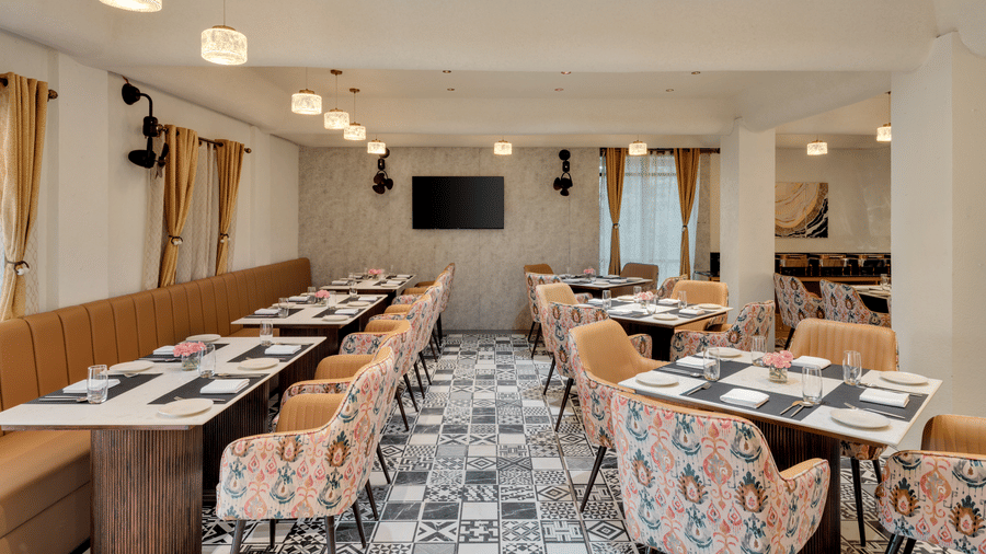 An indoor restaurant with padded banquette seating and patterned chairs and flooring, with recessed lighting and a television mounted on the wall | Voyage Eastin Suites