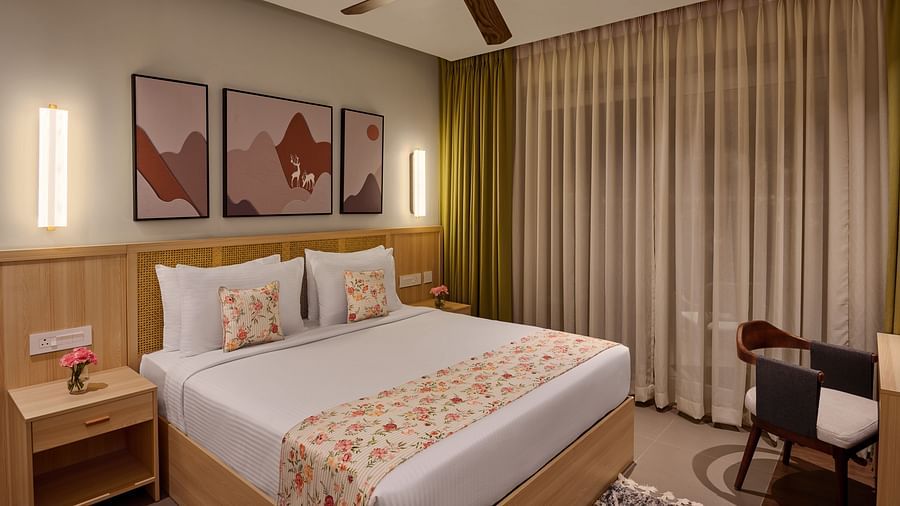 Cosy hotel room featuring a double bed with floral bedding, modern wall art, warm lighting, a ceiling fan, and floor-to-ceiling curtains. A small work desk and chair are placed beside the window - Voyage The Solitaire Bliss.