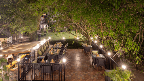A dimly lit outdoor dining setting at night, with multiple tables illuminated by warm lights at The Golden Tusk, Jim Corbett