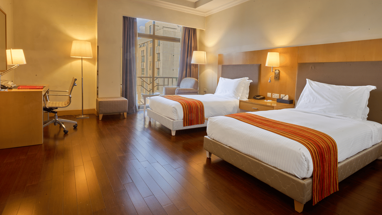 Modern room with twin beds featuring orange-striped runners, bedside tables with lamps, desk area, and warm lighting  - Ramada by Wyndham Addis