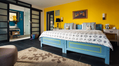 Bright Owl and the Pussycat Hotel in Galle room with a turquoise bed, yellow accent wall, patterned bedding, modern furnishings, and an open bathroom area separated by glass doors.