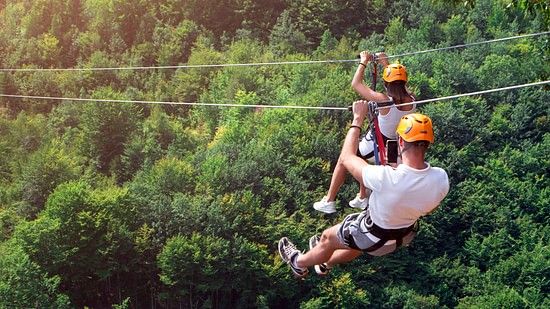 a man and a woman ziplining beside each other during daytime