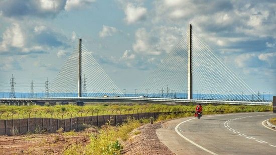A long, modern cable-stayed bridge with two tall towers spanning over a road and landscape.
