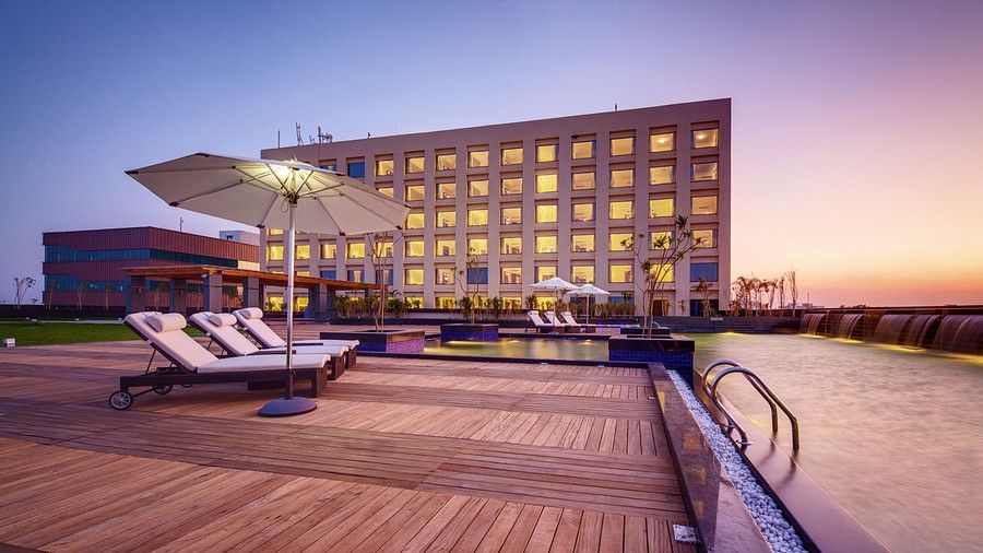 A hotel with a poolside area featuring lounge chairs, umbrellas, and a scenic sunset backdrop - Balaji Sarovar Premiere, Solapur