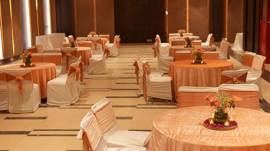 An image of a banquet hall showcasing several elegantly decorated round tables and chairs, illuminated by soft ambient lighting.