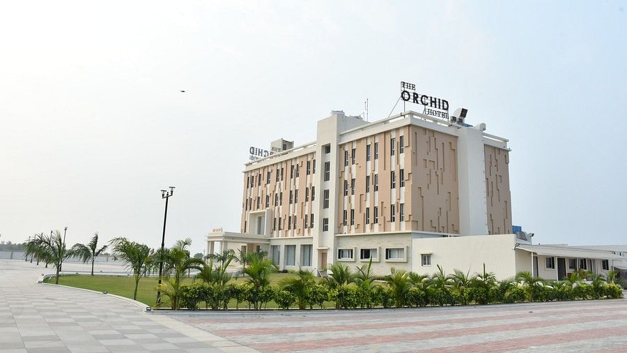 Facade image of The Orchid Hotel, Jamnagar with tiled pathway and manicured garden in view