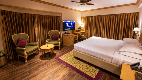 A room with a double bed, wooden furniture seating area with green & brown accents at The Clarton. One of the finest Kodaikanal rooms near lake.
