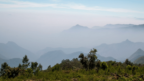 scenic view of the mountain ranges filled with mist cover and blue sky in the background