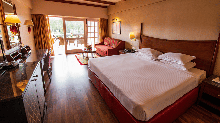 An image of a bedroom featuring a double size bed, a sofa , work desk and chair, and a cabinet table  at The Carlton, Kodaikanal