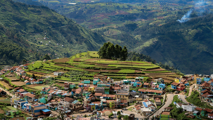 Panoramic view of terraced hills with a densely packed village in the foreground, set against layered mountain ranges in Kodaikanal, Tamil Nadu.