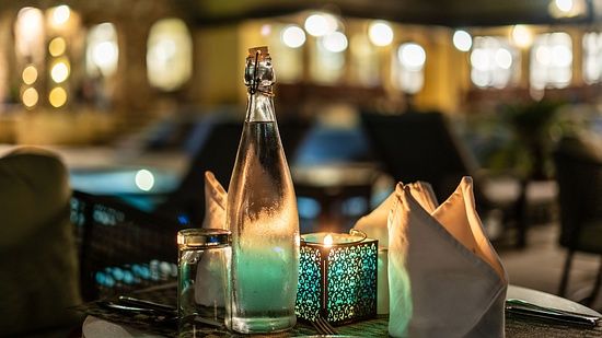 A candlelight dinner table set with a lit candle, tissues, and a glass bottle