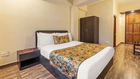 Comfortable hotel room with a double bed, floral yellow bedding, bedside table, wardrobe, and wooden flooring near the entrance door - Summit Namnang Courtyard & Spa, Gangtok