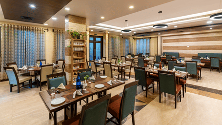 A spacious dining room at Navidya Restaurant featuring modern wooden furniture, polished floors, and large windows that fill the space with light - Amantra Comfort Hotel
