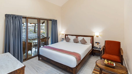 Bedroom of a Luxury Family Suite at Aranya Vilas by Mertia Hospitality featuring a plush bed, wooden furnishings, seating area, and glass doors opening to a private balcony.
