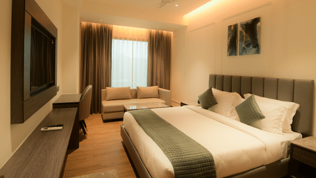 A spacious room with a comfortable king size bed, a television, a sofa near the window, and a study desk at Awesome Palace, Guwahati Airport.