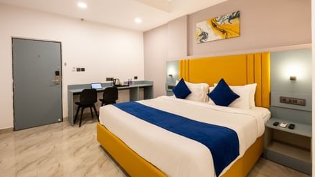 Overview of a modern Premium Room with a bed featuring blue accents, a work desk area, and a door on the left  - Beestay Hotels Financial District, Hyderabad 