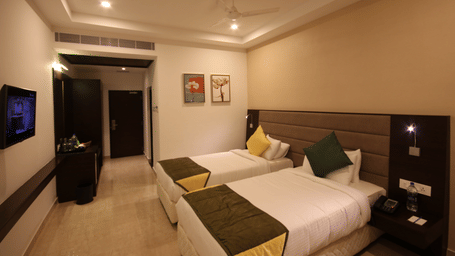 A Premium Room at Khanna Fiesta, Vellore, with twin beds, a nightstand, floral wall art, and polished marble flooring.
