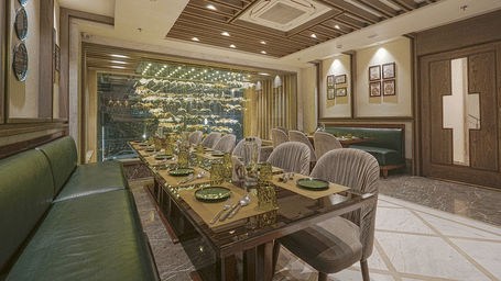 Cafe Blusalz dining area at BluSalzz Residence, Amritsar, with long wooden table, green booth seating, grey chairs, framed wall arts, and large window