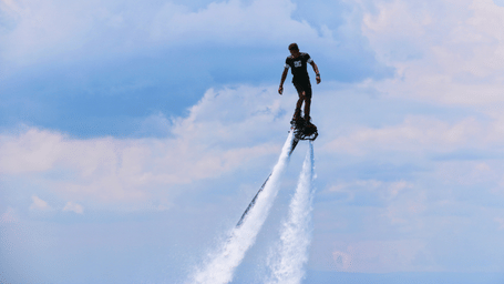 A man flyboarding with bright and clear sky behind him.