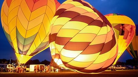 Three brightly coloured hot air balloons are illuminated at night, ready for takeoff.