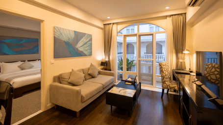 Living area in the Two Bedroom Family Suite at Central Mansions, Phnom Penh featuring a sofa, coffee table, television, and large arched windows.