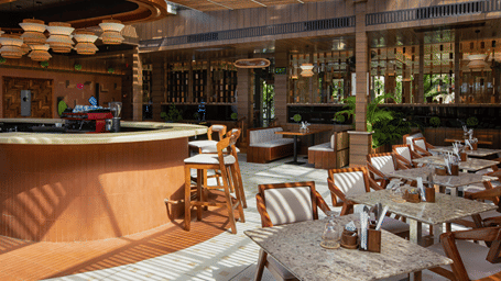 5th Bistro Cafe & Bar in Havelock featuring a beautifully designed interior and dining area with wooden tables and chairs, suspended lighting fixtures, and tropical greenery. The space has a relaxed, elegant atmosphere - Coral Reef Resort & Spa, Havelock