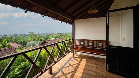 An image of a balcony with a lush view, shot from a corridor, and a fan in the shot.