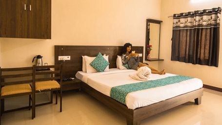 A guest room with a double bed, chairs, and dressing area, with a woman seated at Daksh Resort & Amusement Park, Sasan Gir.