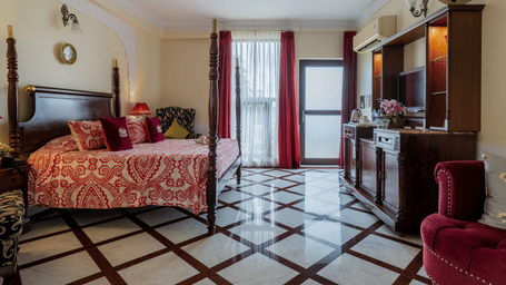  Bedroom with floral bedspread, wooden furniture, and doors opening to balcony at Dera Rawatsar, Jaipur.