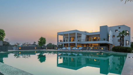 Facade view of DLS Forest Vines Resort with its reflection shimmering on the swimming pool under a clear sky.