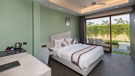 A spacious room at DLS Forest Vines Resort, complete with a large bed, bedside table, table and chairs, and a glass door opening to the balcony.