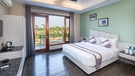Spacious room at DLS Forest Vines Resort featuring a large bed, a bedside table, and a large glass door leading to the balcony.