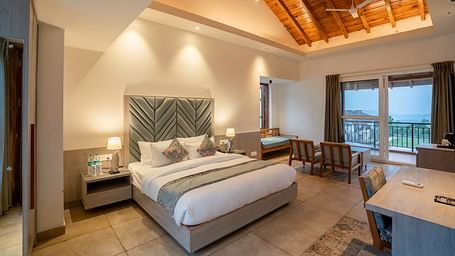 A modern hotel room with a king size bed, a seating area, and a view of the lush green outdoors.