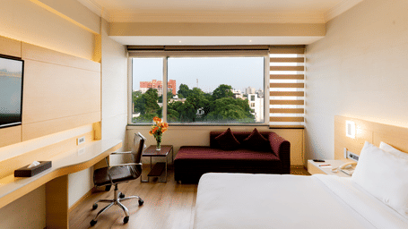 A spacious Superior Room at Gemini Continental with a bed, a seating area next to a large window, a working desk, and a wall-mounted TV.