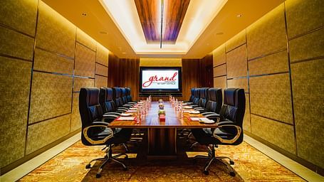 A modern conference room with a large table, executive chairs, and a presentation screen
