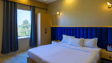 A room with a large bed, a headboard, a window with curtains, and warm lighting.